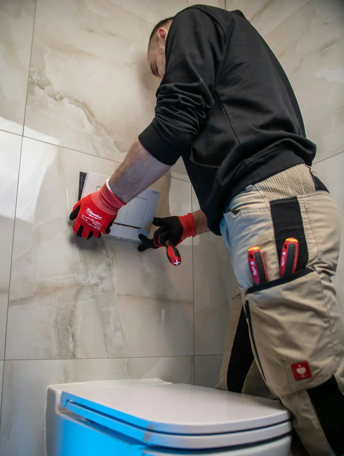 Szerelő piros kesztyűben a WC öblítőjénél dolgozik